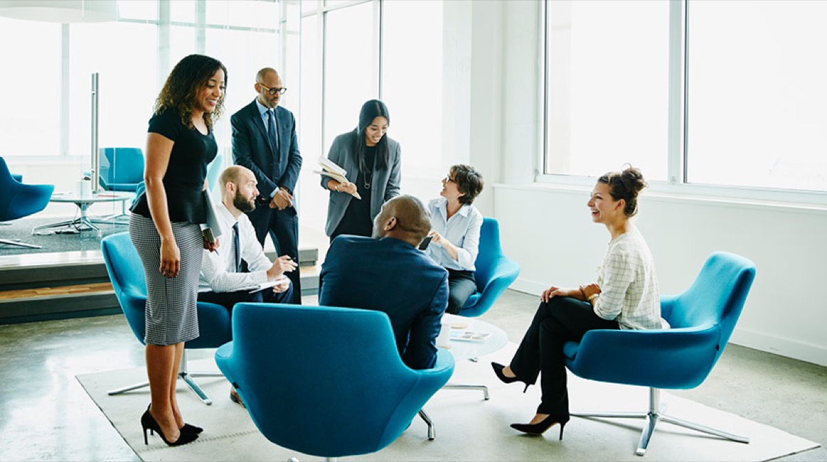A group of colleagues talking together in blue armchairs in a bright office