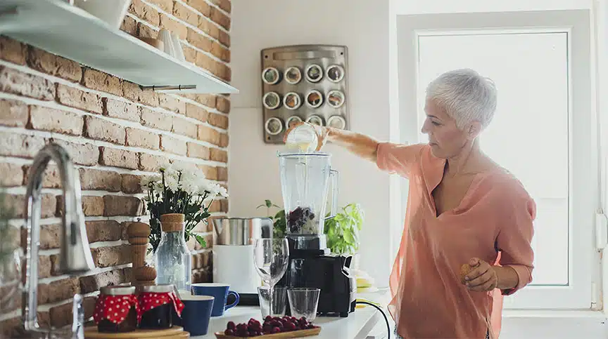 Older Caucasian woman making smoothie in kitchen as she considers how to boost brain health and leadership effectiveness