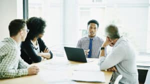 Businessman leading meeting with clients and colleagues in office conference room discussing leadership competencies
