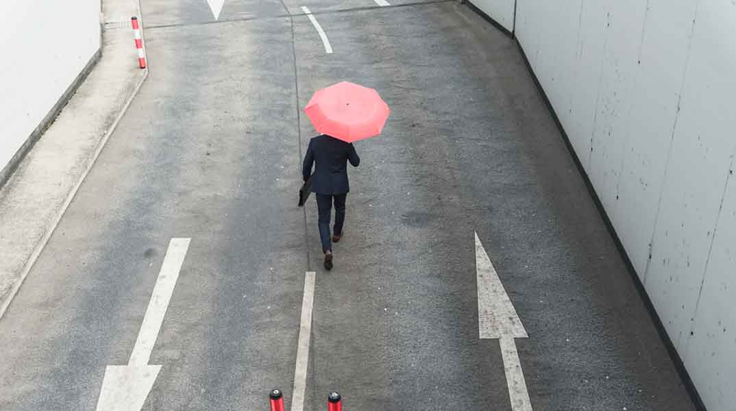 Person walking in the rain; metaphor demonstrating the importance of investing in development in downturns or protecting leadership development budgets during economic uncertainty or recessions