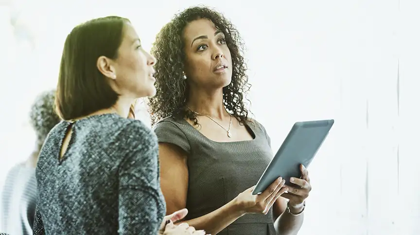 A leader holds a tablet while she and her colleague contemplate the challenges of leadership and AI training